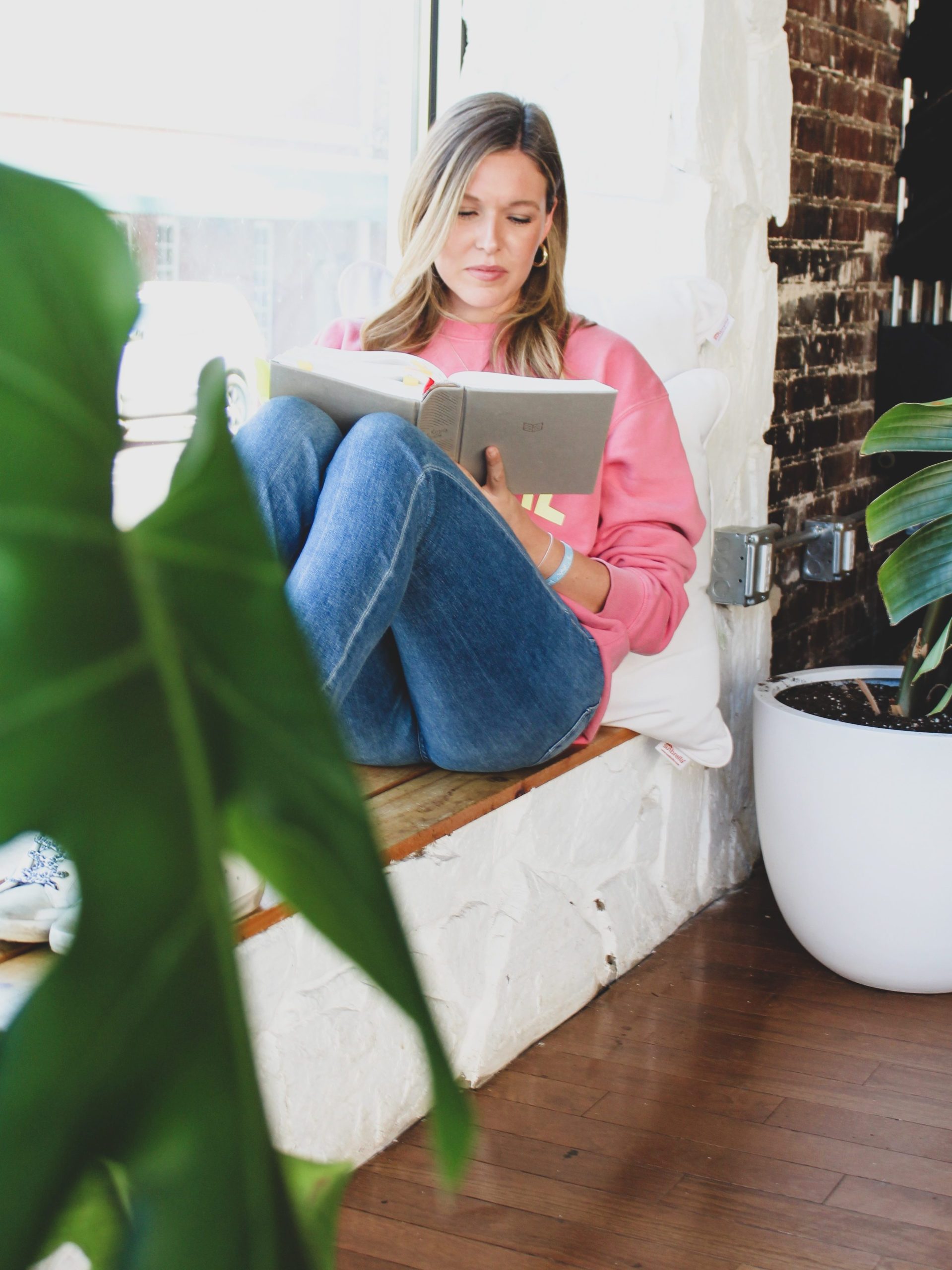 Girl wearing pink sweatshirt reading bible by a window. God's word revives & refreshes.